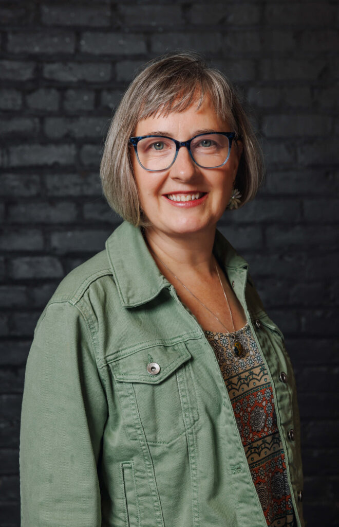 sue standing against dark background in green jacket
